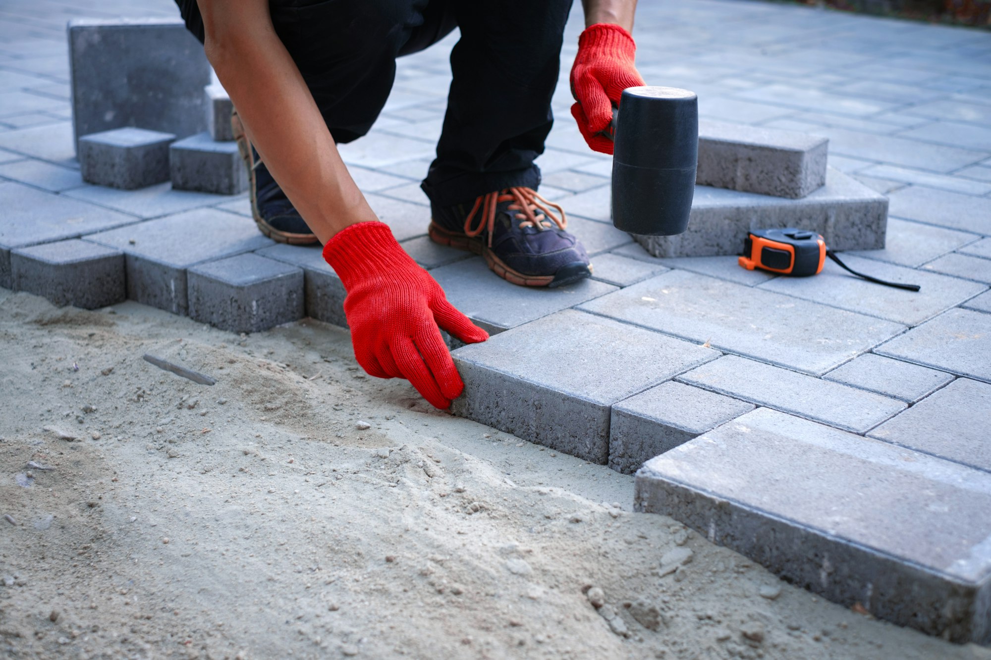 The master in yellow gloves lays paving stones